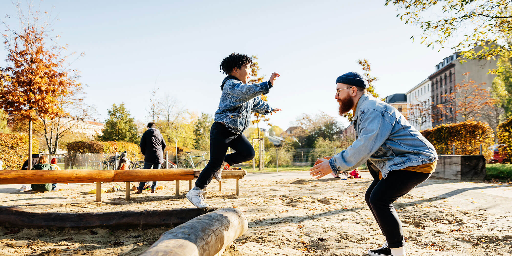 A son leaps from a piece of playground equipment into the arms of his father