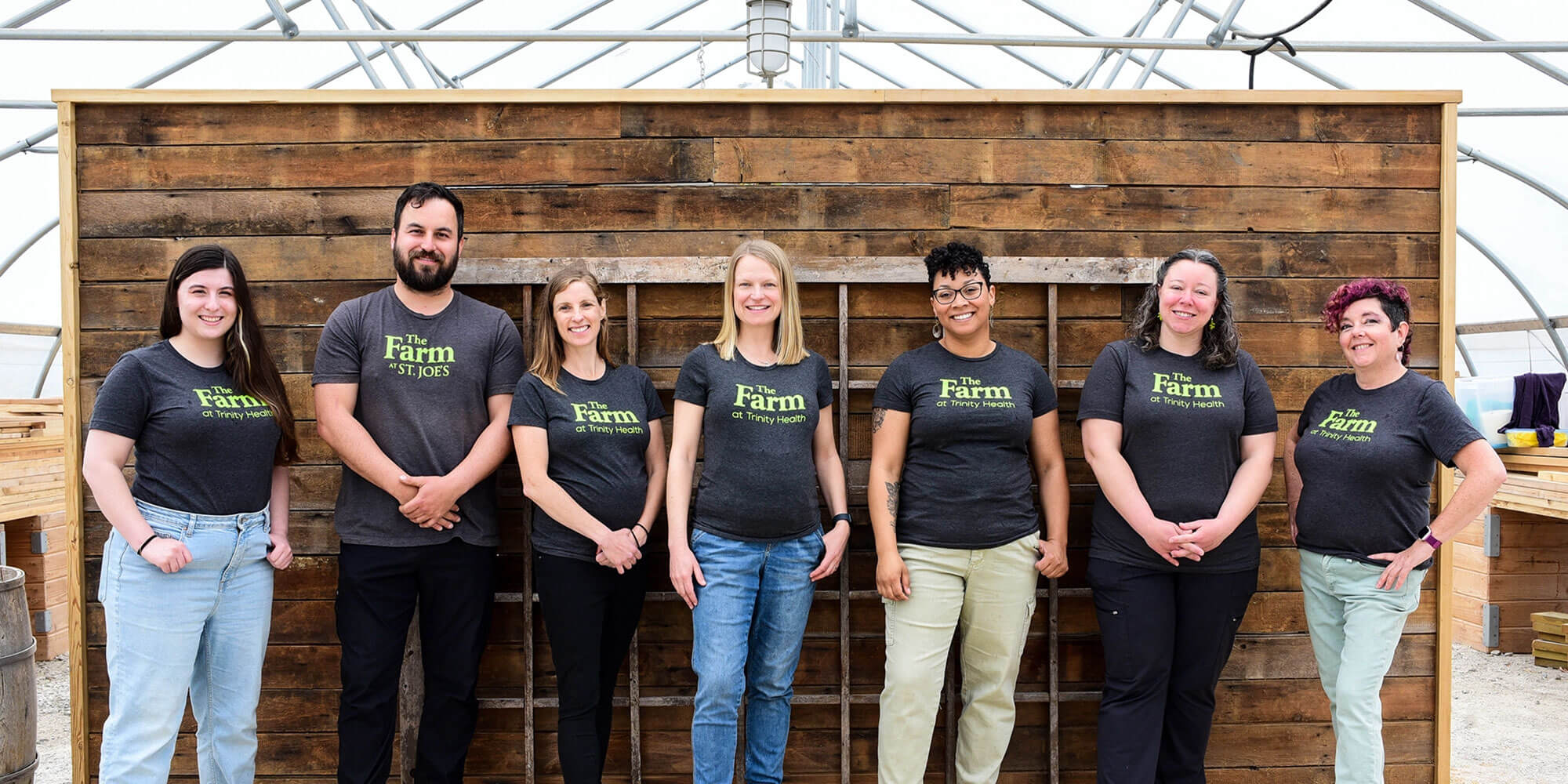 Employees of The Farm at Trinity Health stand in front of a wooden background