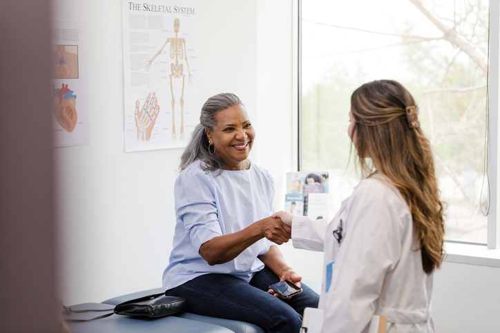 A smiling woman sitting in a doctor's office, shaking hands with her doctor