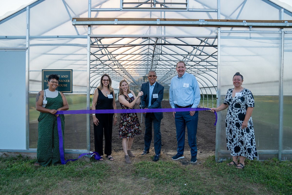 Staff standing in front of greenhouse with ribbon and giant scissors