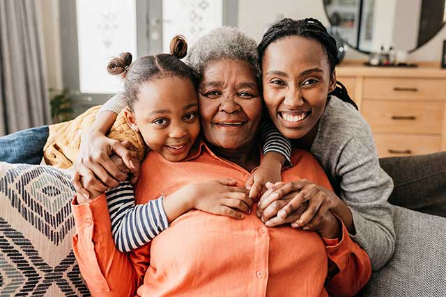 Three generations of women embrace on a couch, smiling at the camera