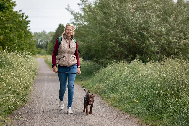 A middle-aged woman in a vest walks her puppy along a park path