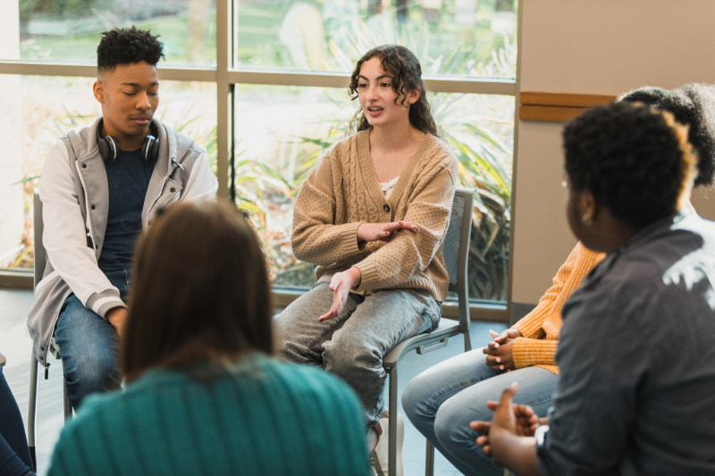 A group of young adults seated in a circle, actively participating in a discussion or group activity.