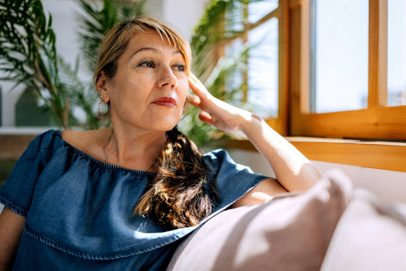 Middle aged woman sits on a couch looking out the window