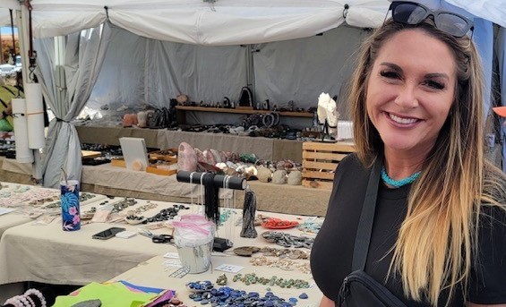 Stephanie smiles standing next to a craft booth outdoors