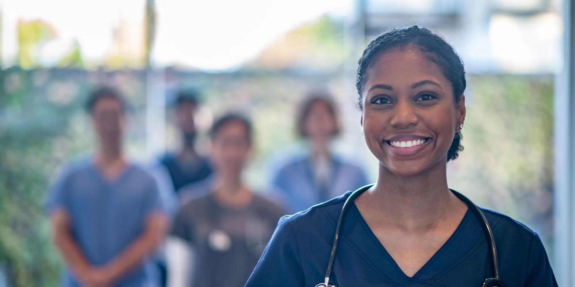 A group of residents stands in a hospital hallway. One woman stands closer to the forefront, smiling.