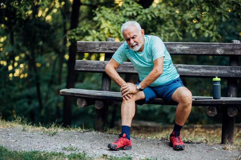 older man with knee pain on bench