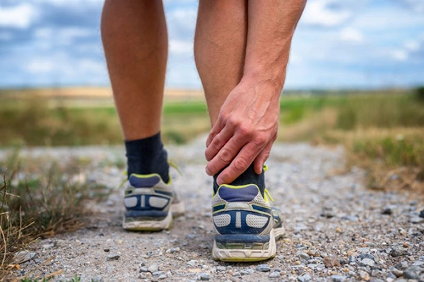 A man leans down and grabs his back right ankle on a hiking path