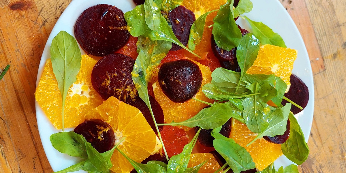 A white plate topped with mixed salad greens, beets, grapefruit, and orange slices on a butcher block countertop.
