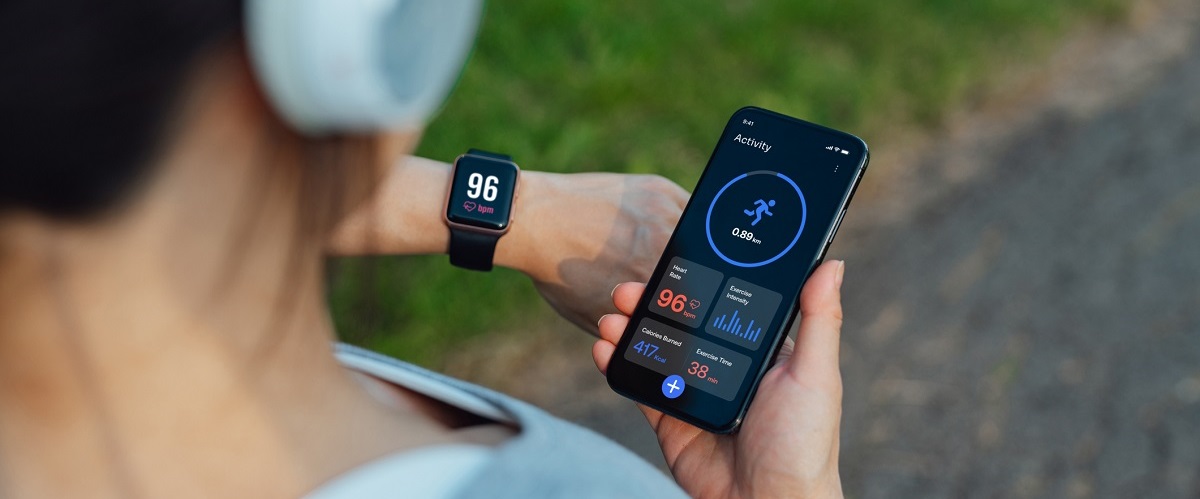A person exercising outside looks at their smart watch and syncs the information to their smart phone.