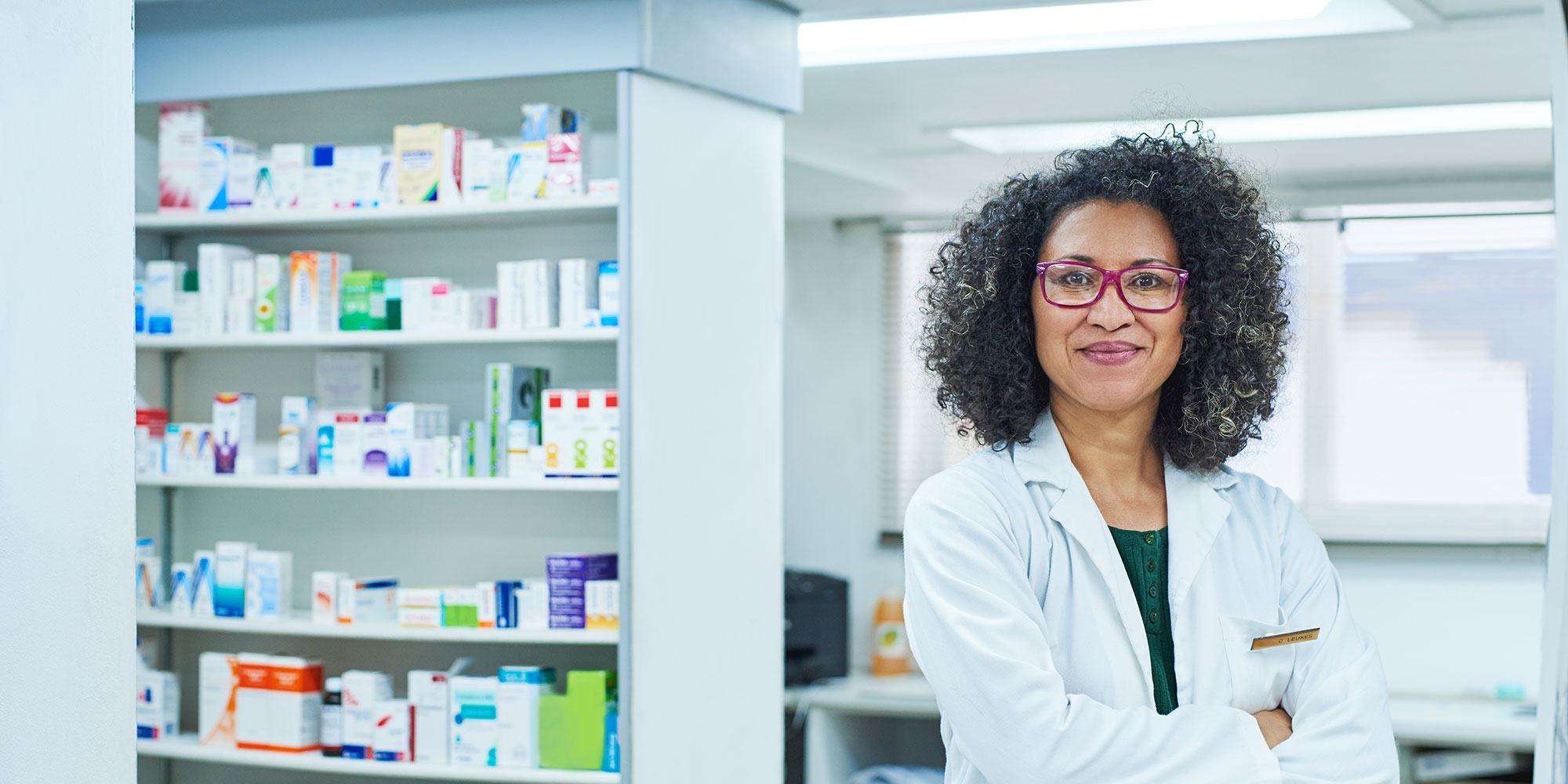 A pharmacist stands with her arms crossed looking professional