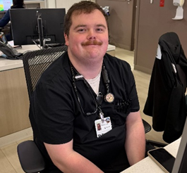 Tyler in scrubs sitting at nurses' station